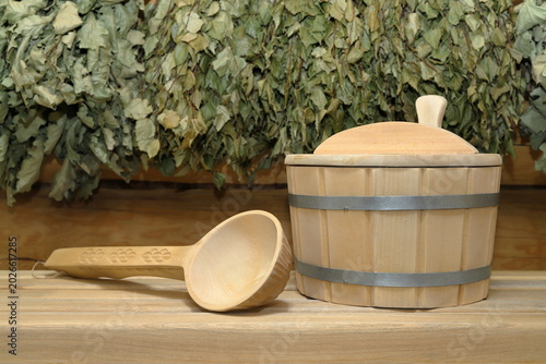 Foto A wooden vat and a wooden ladle are on a plank bench on the background of a log wall with hanging on it a set of a dry birch and oak brooms