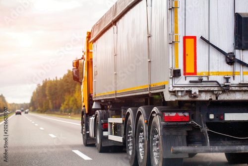 Large semi truck trailer transportation on asphalt highway road at sunset sky driving cargo delivery logistics freight industry commercial vehicle moving goods