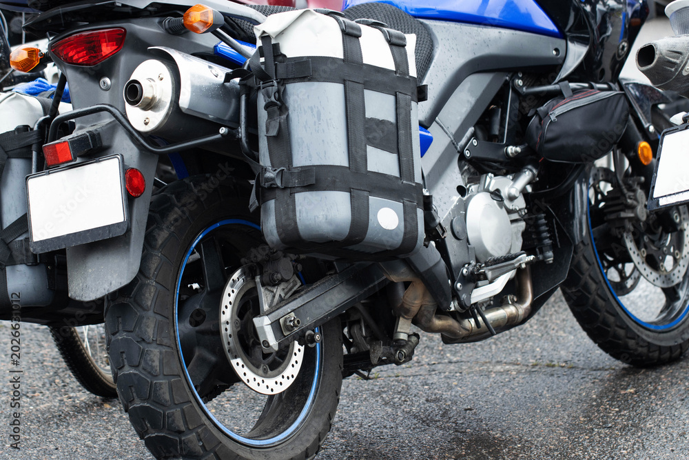Fototapeta premium Adventure touring motorcycle parked on wet asphalt road surface. Close up view of rear wheel, exhaust pipe, taillight, and luggage bags for long distance travel.