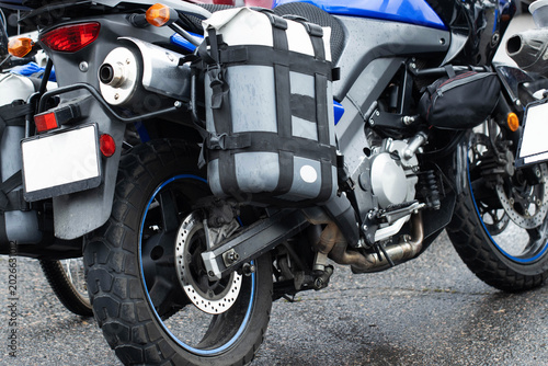 Adventure touring motorcycle parked on wet asphalt road surface. Close up view of rear wheel, exhaust pipe, taillight, and luggage bags for long distance travel.