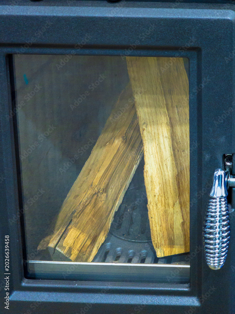 Fototapeta premium Modern Black Cast Iron Wood Burning Stove with Chopped Logs Inside Glass Door