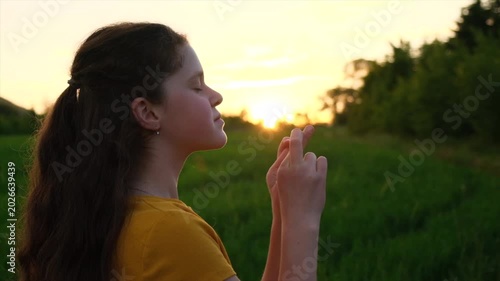 Preteen girl keep fingers crossed, making wish, eyes closed,  in park during warm summer sunset. Beautiful child praying, hands folded in prayer concept for faith, spirituality, worship and religion