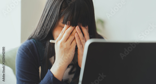 Tableau sur toile Stressed asian woman covering face while using laptop at home, suffering from ey