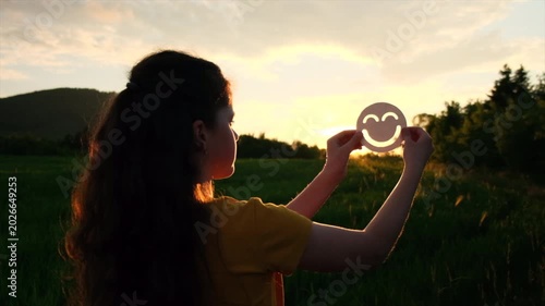 Close up of preteen girl holding happy smile face on background epic sunset in mountains at summer time, good feedback rating and positive customer review, satisfaction survey, mental health