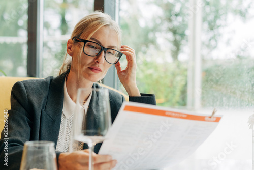 Fotografi Business Woman wearing glasses sits in a restaurant and makes a choice from the menu card