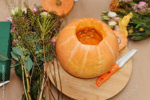 Pumpkin prepared as a vase for floral arrangement. Florist creating autumn centerpiece with flowers and foliage. Preparation for thanksgiving decor, seasonal botanical hobby project.