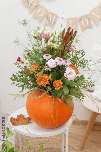 Autumn flower arrangement in pumpkin vase. Colorful floral bouquet on table for Thanksgiving celebration. Creative floristics design with seasonal plant and foliage for home decor.