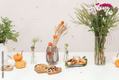 Florist arrangement with pumpkins and wheat on table. Seasonal autumnal decoration with flower bouquet and snacks. Cozy home interior design for thanksgiving celebration and fall event.