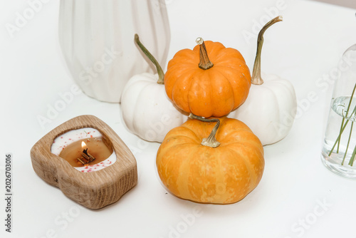 Small orange and white pumpkins arranged with a rustic wooden candle on a table. Fall home decor flat lay for harvest festival celebration. Autumn seasonal interior styling concept.