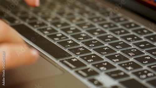 Finger pressing key on backlit Cyrillic and Latin laptop keyboard