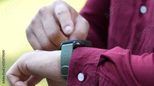 The close up of a man wearing a smartwatch on his left wrist and using this device outside. Electric gadget and a user shot on blurry background.