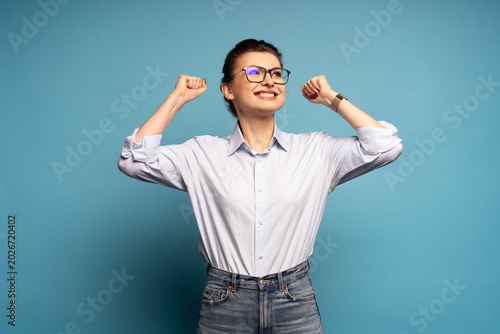 Extremely happy woman standing with raised clenched fists, winning lottery, celebrating her success isolated on blue