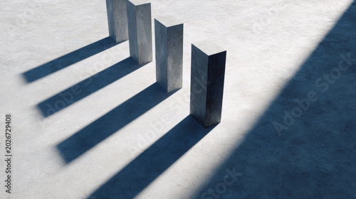 Four vertical concrete pillars casting long shadows on a smooth gray surface under bright sunlight, creating a minimalist architectural composition