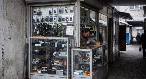 Street electronics repair kiosk in a weathered urban passage, Eastern Europe editorial-like