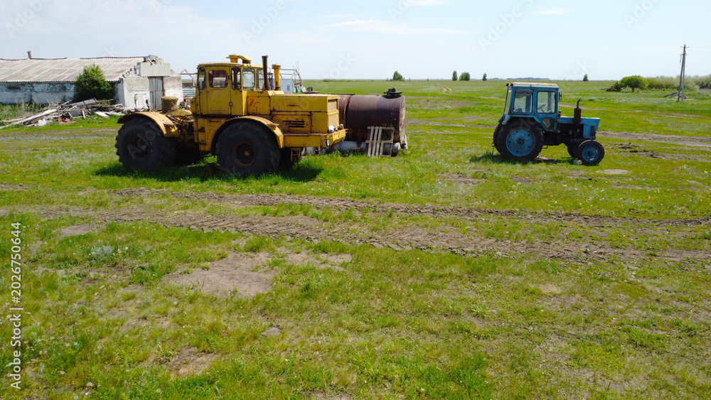 Obraz premium Yellow heavy articulated tractor and small blue tractor in a rural pasture