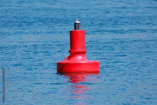Bright red buoy with solar panel floats on calm blue ocean water