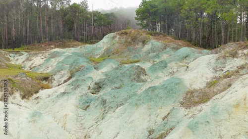 Low-altitude aerial sideways flight past Blue Soil Hills in Sagada reveals intimate close-up of surreal blue-green and white mineral clay mounds framed by misty pine forest