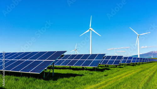 Large solar power plant and wind turbines on a green grass field with mountain view, turbines