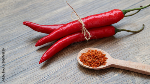 Fotografija Chilli flakes and fresh peppers on wooden background