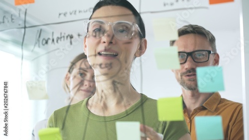Professional team brainstorming project strategy, placing colorful sticky notes on glass board, analyzing data, sharing insights, developing collaborative solutions