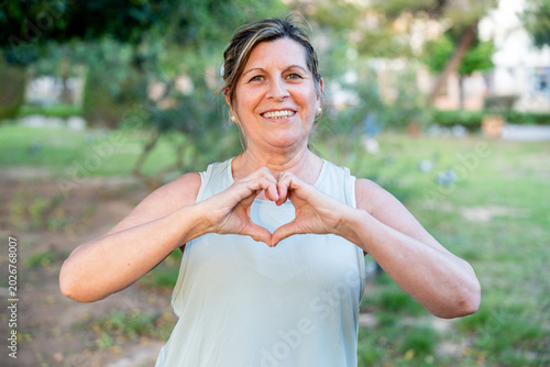 Cuadro en lienzo Senior woman smiling and forming a heart shape with her hands, expressing love a