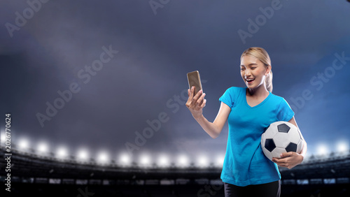 Bild auf Leinwand A cheerful Indonesian southeast asian woman in a blue shirt holds a soccer ball