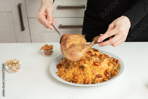 Foto kabsa,roasted chicken leg being placed over a large plate of spiced rice topped