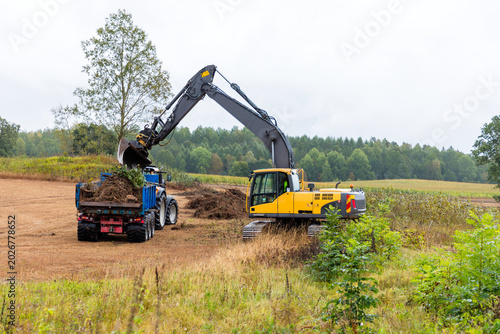 Excavation vehicle loading debris on tractor in rural area