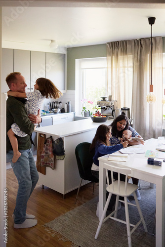 Happy father playing with daughter while mother assisting girl in studies at home
