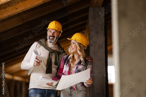 Two Construction Workers Look at Blueprints and Discuss Plans in a Building Site During the Day