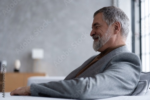 Portrait of handsome bearded mature businessman looking away thoughtfully while sitting on sofa.