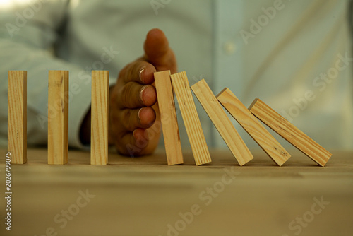 Konstfotografi A hand intervenes to stop a row of falling dominoes, symbolizing risk mitigation