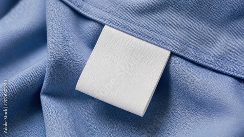 Blank white laundry care clothes label on blue shirt fabric texture background offers a minimalist space for branding and garment care instructions