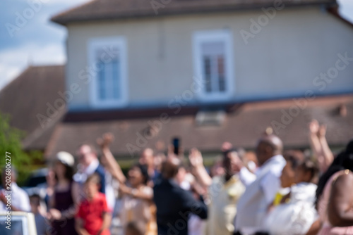 Defocused crowd of people gathered at an outdoor public event in front of a city building in daylight