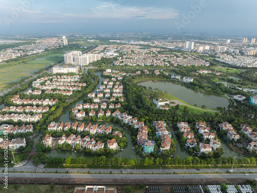 Drone perspective over tree-lined villa compounds and lakeside residences in Long Bien, Hanoi under soft evening sunlight.