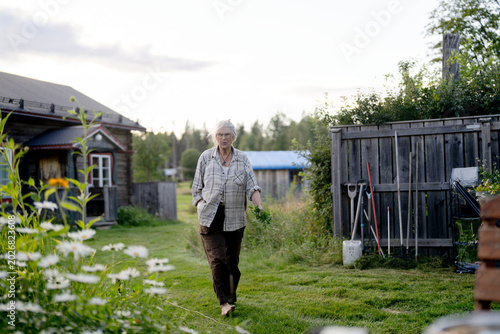 Full length of senior woman holding harvested plant walking with hand in pocket at back yard