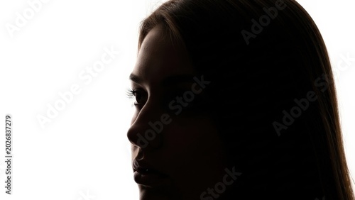 Mysterious profile of a young woman's silhouette, capturing her thoughtful expression against a stark white background, emphasizing shadow and introspection