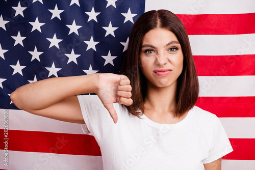 Canvas-taulu Young woman thumbs down in front of american flag wearing white tshirt conveying