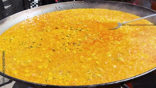 Traditional Spanish paella cooking in large pan outdoors with bubbling saffron rice and seafood ingredients, authentic Valencia cuisine prepared at street food festival in sunny daylight