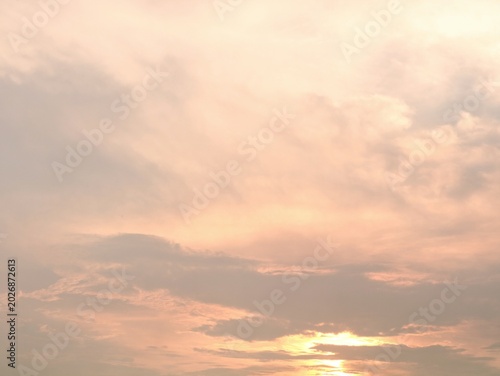 A serene and beautiful sunset sky filled with soft pastel orange and peach colored clouds. The gentle sun glows from the horizon, creating a peaceful, warm, and dreamy atmospheric background