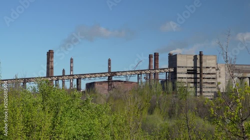 Large industrial factory complex with railway infrastructure, chimneys and industrial buildings surrounded by green vegetation. Static 4K footage of heavy industry landscape.