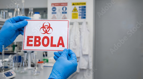 Gloved hand holding ebola biohazard warning sign in laboratory setting
