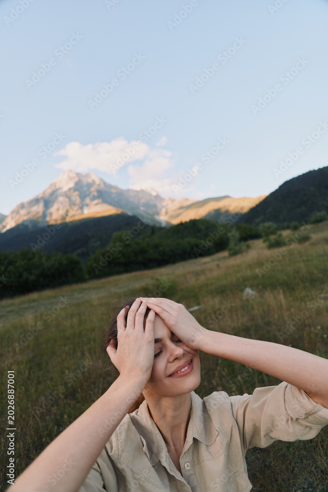 Fototapeta premium Cheerful woman outdoors, enjoying sunlight, relaxed pose, hands on head, smiling expression, natural colors, wide field scenery, distant mountains, calm breeze
