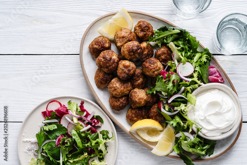 Meatballs served green salad and yogurt based dip on tray, comfort food