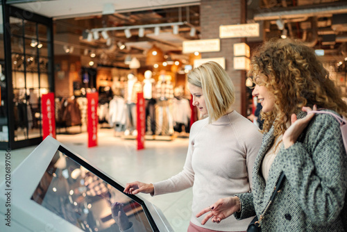Photos Women using interactive touch screen kiosk in shopping mall