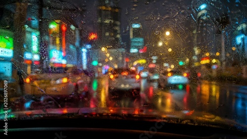 windshield. Nighttime cityscape viewed through a rain-streaked windshield, neon lights blending with street reflections. travel magazines.