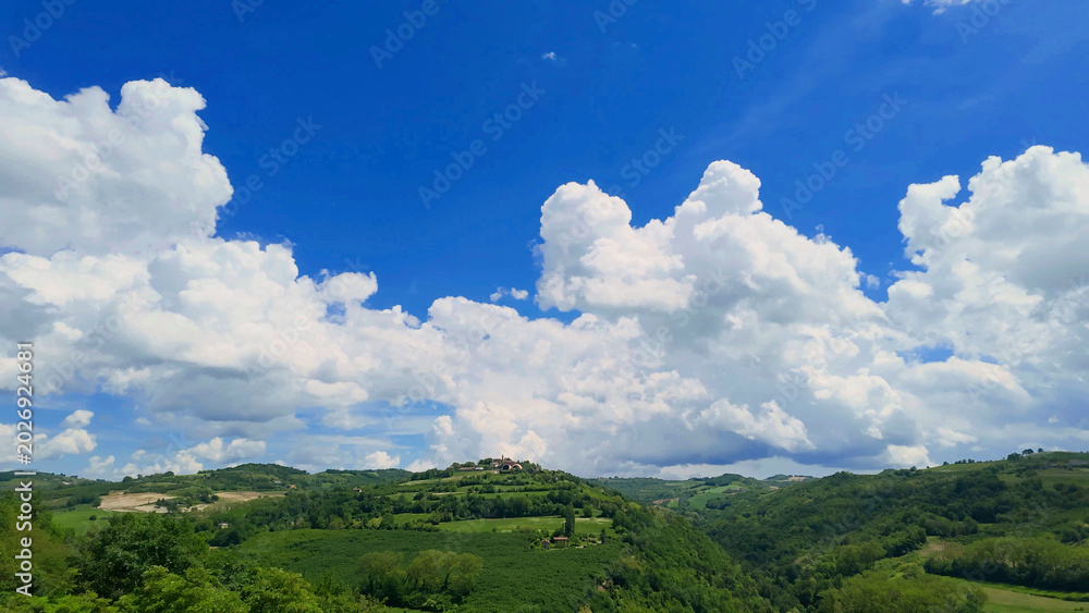 Fototapeta premium Fluffy White Clouds Over Rolling Green Hills and Vineyards in Piedmont Italy