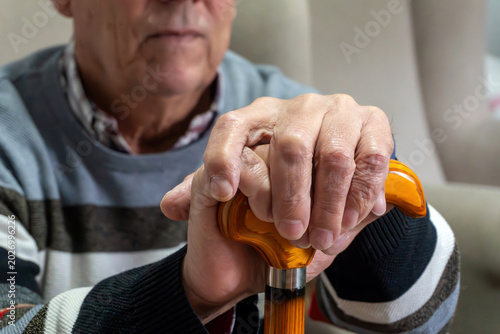 Tableau sur toile Elderly man holding a walking cane, showing wrinkled hands, representing aging,