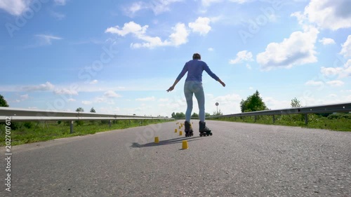 An adult woman is learning to roller skate. She is using yellow cone chips.