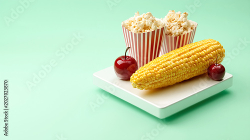Corn on the cob with popcorn and cherries on pastel background
